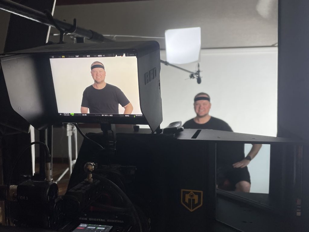 Video production interview setup showing a smiling man on camera, viewed through a professional video camera monitor.