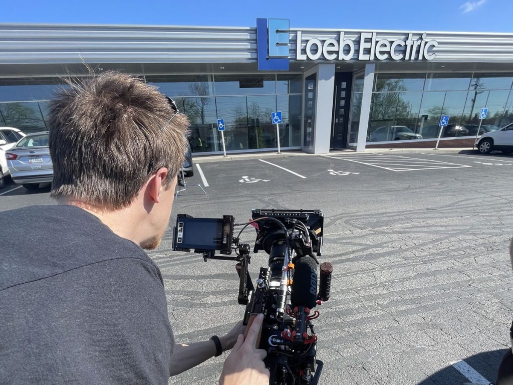 Corporate videographer filming outside the Loeb Electric building using professional video equipment.